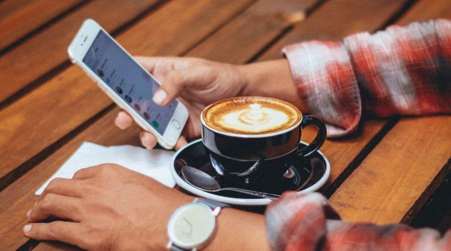 Photo of a man drinking coffee while browsing a restaurant menu on his phone